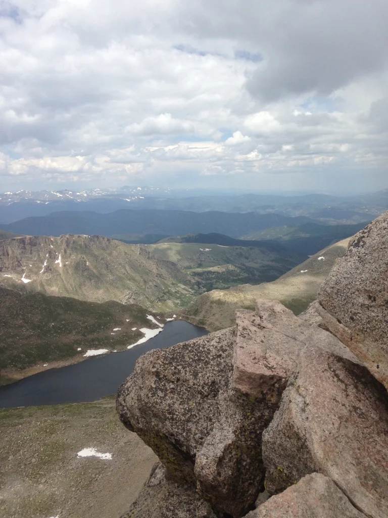 Granite outcrop above an alpine lake and rolling mountain ridges under clouds