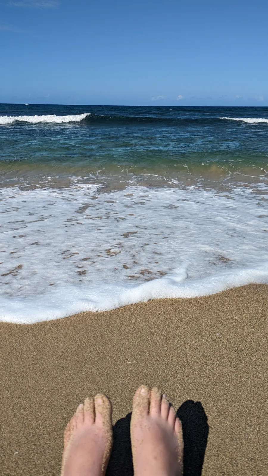 Bare feet in the sand as a wave washes up the beach