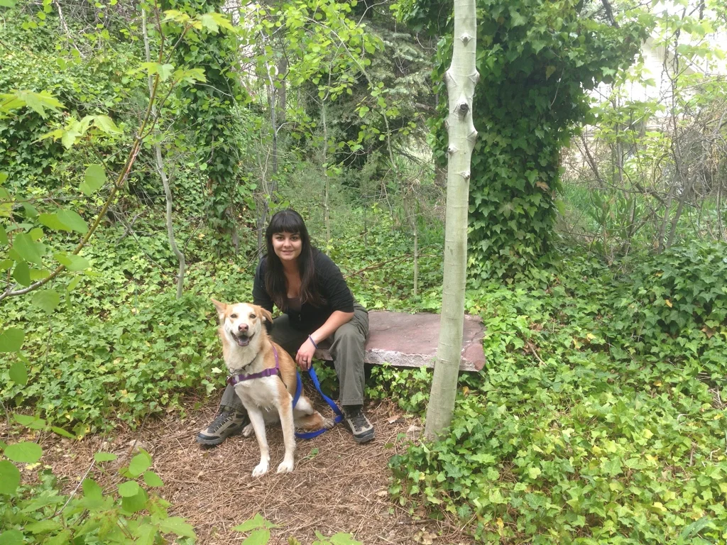 Abigail sitting on a forest path with Moya, her orange husky service dog and field partner
